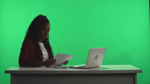 テレビニュース番組 緑の画面に対して暗いスタジオでは アフリカ系アメリカ人のテレビのプレゼンターは ノートパソコンと紙の上のプログラム計画を使用して放送の準備をします 火がつき — ストック動画
