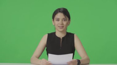 Asyalı bir TV sunucusu masaya oturur ve elinde tuttuğu bir gazeteden bilgi okur. Yeşil ekran geçmişi olan bir TV haber programı. Yayın ağı haber stüdyosu konsepti. Reklamcılık