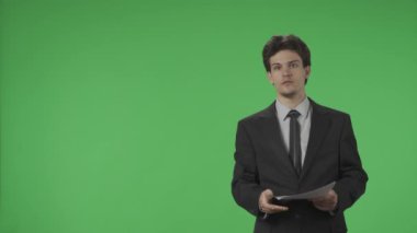 TV Canlı Haber Programı. Stüdyoda elinde kağıtlarla yeşil ekrana karşı TV sunucusu olarak. Profesyonel spiker güvenle konuşuyor ve yeşil ekrana işaret ediyor. Reklam alanı