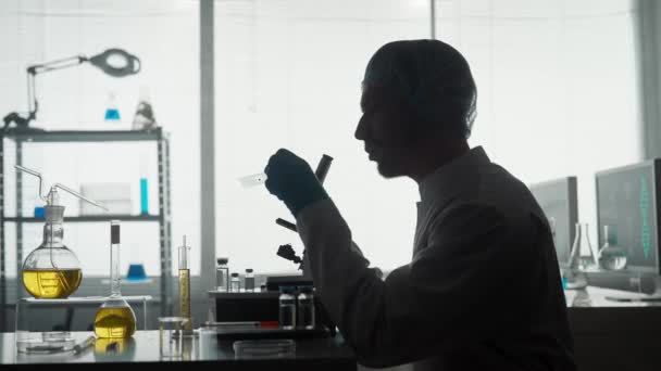 医学科学实验室研究实验室里的一位年轻科学家用显微镜检查了微制剂样品 一个男人坐在一个男人面前的黑暗轮廓侧视图 — 图库视频影像