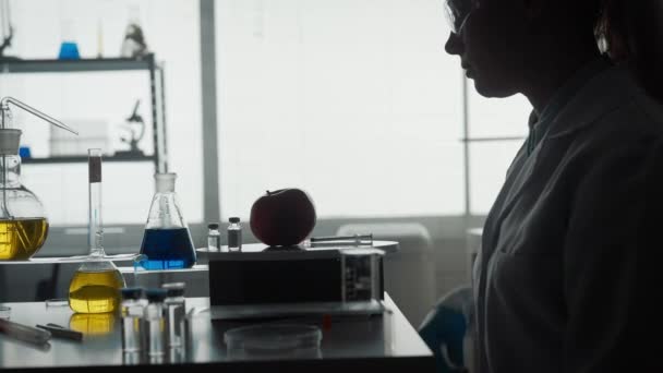研究室で注射器を手にした女性科学者の暗いシルエット 女性は注射器で赤いリンゴに液体を注入します 女性は果物の変更 濃縮に取り組んでいます — ストック動画