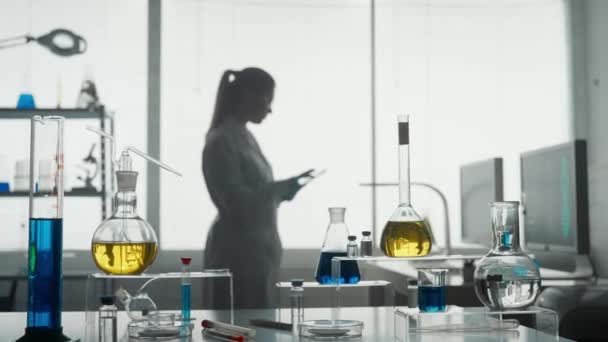 現代医学研究所 女性研究者は研究室でタブレットを使う 女性はフラスコ内の緑色の液体を分析します 背景がぼやけている 医学の高度な科学研究所 — ストック動画