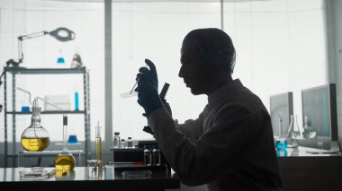 Tıp bilimi laboratuvarı. Bir insan araştırmacı cam kaydırağa bir örnek uygular, pipet kullanarak bir mikro hazırlık. Laboratuvarda mikroskobun yanında bir erkek bilim adamının karanlık silüeti.