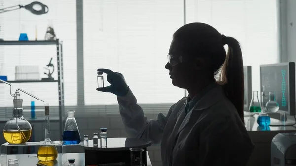 ワクチンの研究開発 ガラスの小瓶を持つ女性科学者の暗いシルエット — ストック写真