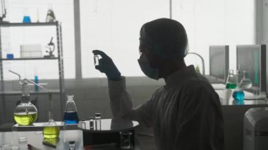 Aşıyı araştırma ve geliştirme. Cam ampul şişeli bir erkek bilim adamının karanlık silueti. Konsept: Hastalık, tıbbi bakım, bilim, anestezi. HDR BT2020 HLG Malzemesi