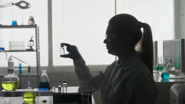 研究和开发疫苗 一个拿着玻璃瓶的女科学家的黑暗轮廓 Hdr Bt2020 Hlg Material — 图库视频影像