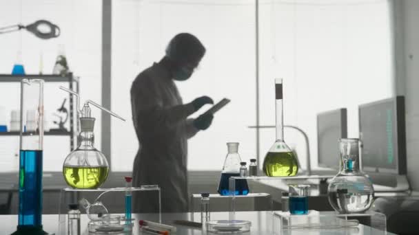 现代医学研究实验室 一名男性研究人员在实验室里使用平板电脑 一个男人分析瓶子里的绿色液体 模糊的背景 医学高级科学实验室 — 图库视频影像