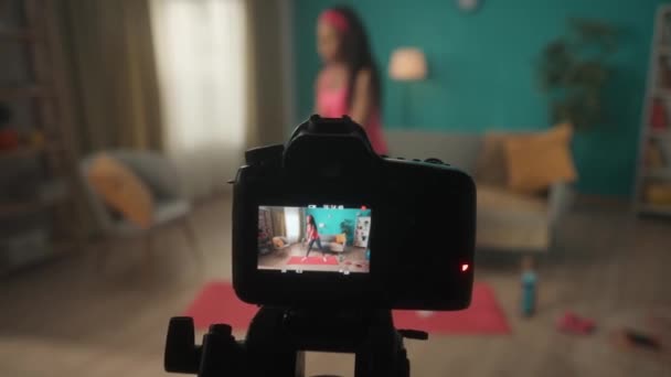 女性トレーナーは オンラインフィットネスビジネスのための新しいコンテンツを記録するためにカメラを使用します リビングで練習をしながらカメラでビデオを撮影する女性 プロ仕様のデジタル機器 — ストック動画