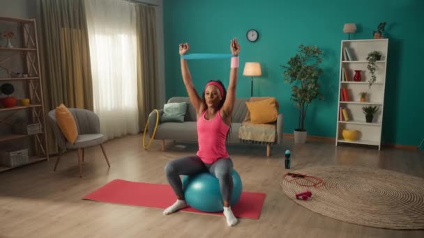 Афроамериканка Сидящая Фитболе Тренирующаяся Группой Сопротивления Гостиной Женщина Спортивном Костюме — стоковое видео