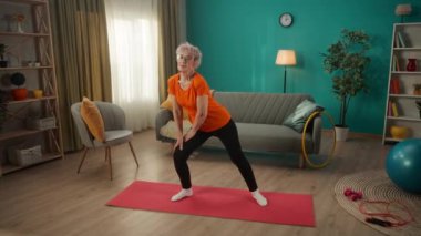 Egzersiz yaparken yan hamleler yapan yaşlı bir kadın. Beyaz saçlı, emekli bir kadın sağlığına dikkat eder, bacak ve kalçalarının kaslarını güçlendirir. Sportif yaşam tarzı, sağlık kavramı