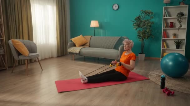여자는 거실에서 고무줄로 운동하는 나이에요 한연로 부인은 다리로 똑바로 바닥에 — 비디오