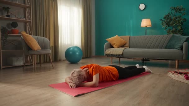 筋疲力尽的老年妇女躺在地板上 躺在一块运动垫上 做了艰苦的锻炼后休息 这个女人把头靠在手上 闭上眼睛 休息一下 做完一项积极的运动后暂停一下 疲劳症 — 图库视频影像