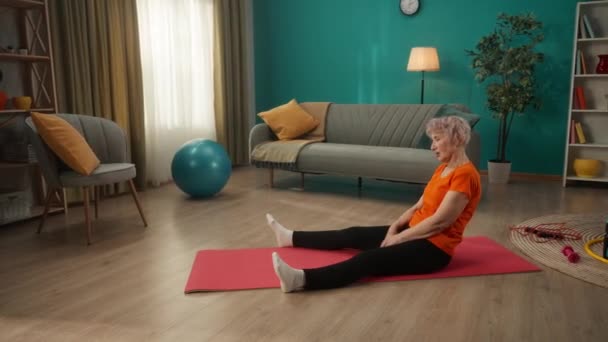老年妇女在锻炼后做伸展运动 一个退休的女人坐在一个伸直腿的运动垫上 伸手去拿袜子 侧视图 运动生活方式 健康的概念 — 图库视频影像