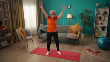 Spor giyimli yaşlı bir kadın evde mavi bir halka çeviriyor. Vücudunu formda tut. Sportif yaşam tarzı, emeklilik, sağlık, sağlık. Yavaş çekim