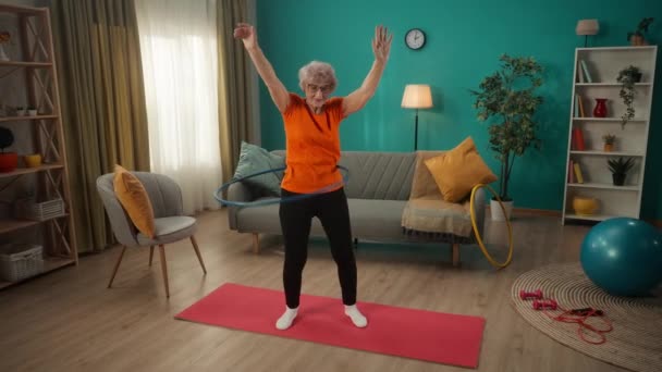 スポーツウェアを着た年配の女性が家で青いフープを回している 体を調子よく保つこと スポーツライフスタイル ウェルネスの概念 スローモーション — ストック動画