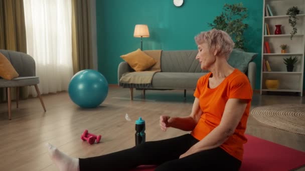 Starsza Kobieta Zmęczona Codziennym Treningu Siedzi Macie Sportowej Salonie Kobieta — Wideo stockowe