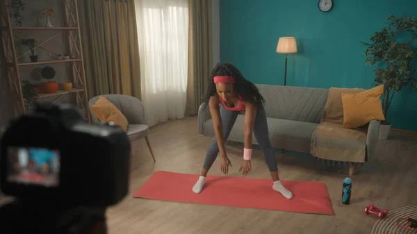 女教练员在专业数字设备前做向前弯的动作 非裔美国妇女使用相机记录新内容的在线健身 网上学习的概念 视频博客 — 图库照片