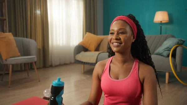 一位穿着运动服 心满意足的非洲裔美国女人的画像 以及客厅里的头巾 都是特写 微笑的女运动员手里拿着一个水瓶 — 图库照片