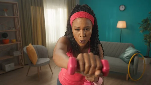 运动的非洲裔美国女人在家里用哑铃做运动时 动作要靠得很近 一个女人在用哑铃打拳 增强她的手臂肌肉 家庭健康 生活方式的概念 — 图库照片