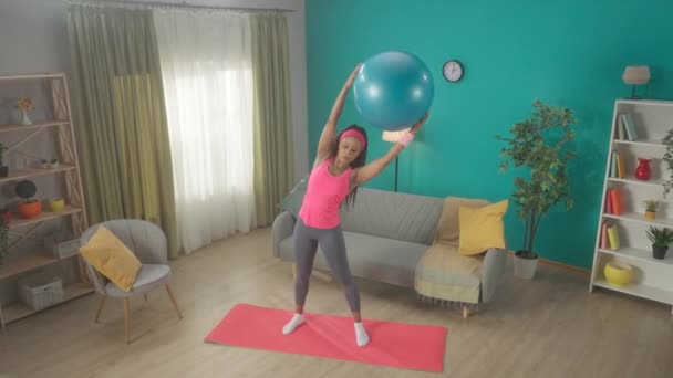 Μια Αφρο Αμερικανίδα Σηκώνει Μια Μπάλα Γυμναστικής Πάνω Από Κεφάλι — Αρχείο Βίντεο