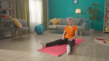 Yaşlı bir kadın antrenmandan sonra esneme hareketleri yapıyor. Emekli bir kadın düz bacaklarıyla bir spor minderine oturur ve çoraplarına uzanır. Sportif yaşam tarzı, refah kavramı. HDR BT2020 HLG Malzemesi