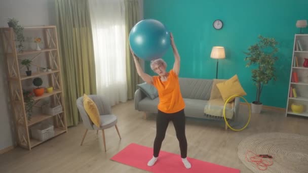 Ηλικιωμένη Γυναίκα Πηγαίνει Για Σπορ Μια Μπάλα Γυμναστικής Στο Σαλόνι — Αρχείο Βίντεο