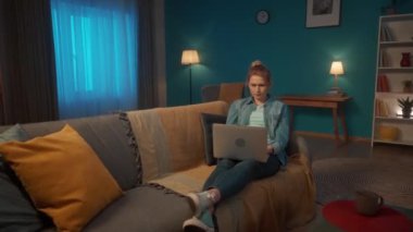 Oturma odasındaki kanepede dizüstü bilgisayarı olan genç bir kadın yatıyor. Yoğunlaşmış yüzlü bir kadın çalışıyor ya da bilgisayarında oyun oynuyor. Yorgun olduğu için gözlerini kırpıyor.