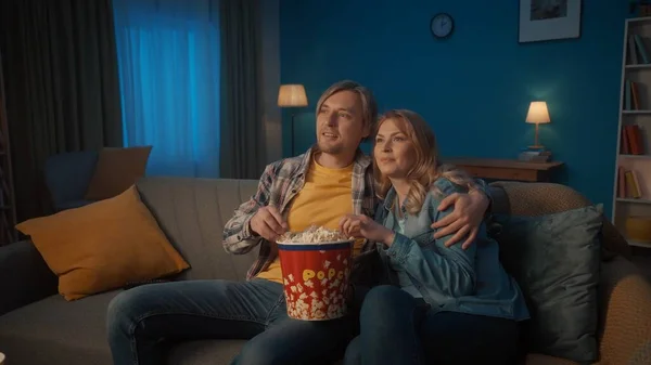 一对年轻夫妇正在看电影 吃爆米花 在客厅里舒服的沙发上拥抱和放松地微笑着 欣赏着电影 — 图库照片