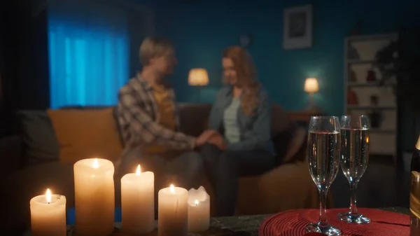 一杯香槟和一个模糊的爱的夫妇的背景 迷恋的男人和女人在客厅的沙发上手牵手 浪漫的烛光晚餐和香槟约会 — 图库照片