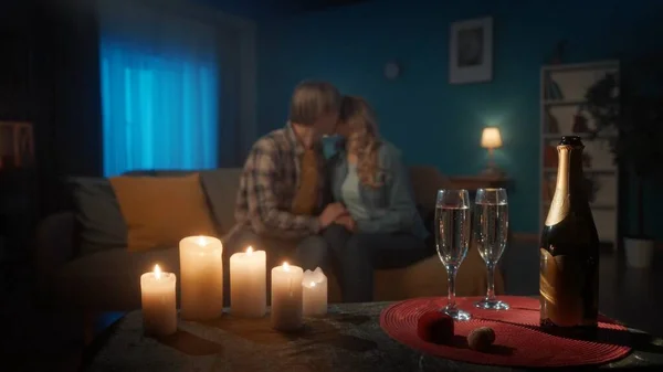 一杯香槟和一个模糊的爱的夫妇的背景 一对恋爱中的男女坐在客厅的沙发上接吻 浪漫的烛光晚餐和香槟约会 — 图库照片