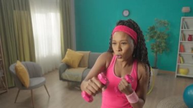 Atletik Afrikalı Amerikalı kadın evde halterlerle egzersiz yapıyor. Bir kadın dambıllarla boks yapıyor, kol kaslarını güçlendiriyor. Spor konsepti, ev fitness, yaşam tarzı. Ağır çekim. HDR