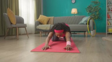 Antrenmandan sonra esneme hareketleri yapan bir kadın. Afrika kökenli Amerikalı bir kadın dizlerinin üzerinde oturuyor, öne doğru eğiliyor, leğen kemiğini geriye doğru çekiyor ve kollarını öne doğru açıyor. Bir kadın sırtı için egzersiz yapar ve...