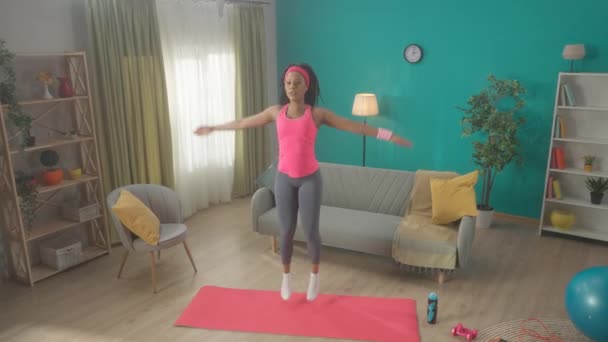 アフリカ系アメリカ人の女性はリビングのジムマットに飛び乗って星をやっています かなり細い女の子は彼女の健康の世話をし 彼女の足とお尻の筋肉を強化します ホームフィットネスのコンセプト ゆっくり — ストック動画