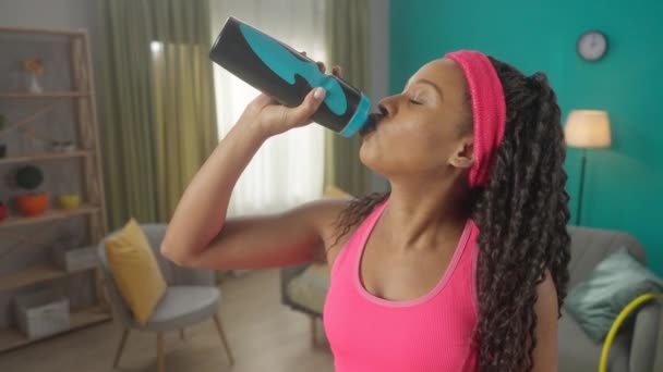 アフリカ系アメリカ人の女性は ワークアウトの後に喉の渇きを癒す 飲料水を楽しんでいます 内容の肖像画は リビングルームに笑みを浮かべて女性を閉じます スローモーション Hdr Bt2020 Hlg材料 — ストック動画