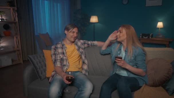 若い夫婦は 夕方にはソファに座って 赤ワインを話し 飲んでいます 女性はその日の出来事を共有し 面白い話 逸話を語ります 二人は楽しそうに笑ってる — ストック動画