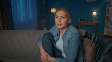Genç bir kadın kanepede bacaklarıyla oturur ve akşamları televizyon izler. Bir kadın bir film izler, bir realite şovu, dikkatle dinler, hikayenin çarpıtılmasına şaşırır. Şaşırmış bir kadının portresi. Yakın plan.