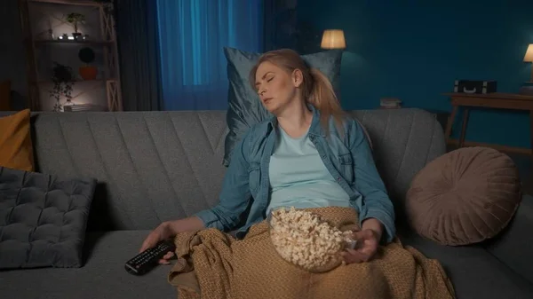 这个年轻的女人在影片中睡着了 一个疲惫的女人睡着了 她坐在沙发上靠得很近 膝盖上放着爆米花 手里拿着遥控器 无聊的电影 — 图库照片