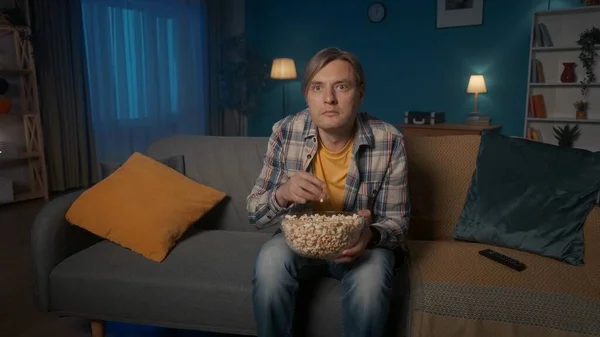 这个人在看恐怖片时吓得直哆嗦 一个男人的画像 傍晚时分 他坐在客厅的沙发上 手里拿着一盘爆米花 — 图库照片