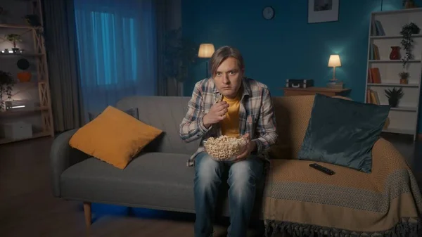 这个人在看恐怖片时吓得直哆嗦 一个人坐在客厅的沙发上 手里拿着一盘爆米花 — 图库照片