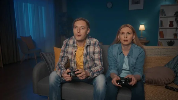 一对年轻夫妇在晚上坐在沙发上与游戏控制器一起玩电子游戏 男人和女人花时间在一起享受游戏 谁会赢游戏概念 — 图库照片