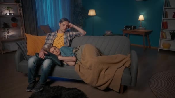 結婚した夫婦は夜遅くテレビを見ながら眠ってしまった 彼の手の中にリモートコントロールを持つ男はソファの上に座って眠りに落ち 女性は男の膝の上に休んで彼女の頭で眠る 退屈な — ストック動画