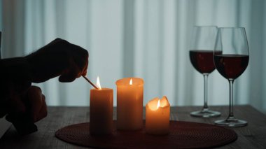 Mum ışığında romantik bir akşam. Mumları kibritle yakan bir adamın elleri. Yanan mumlar ve kırmızı şaraplı bardaklar.