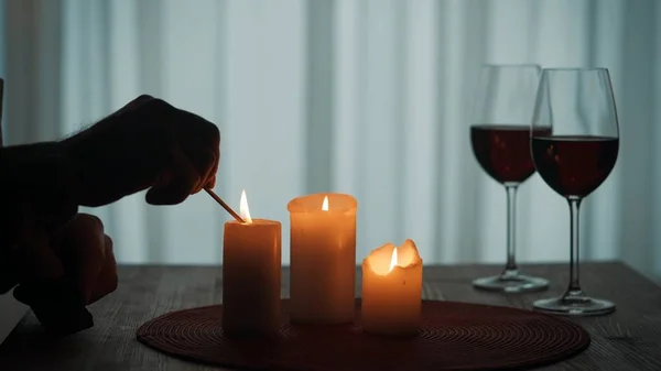 キャンドルライトでロマンチックな夜 試合が終わるとろうそくを灯す男の手 テーブルの上に赤ワインでろうそくとガラスを燃やす — ストック写真