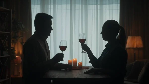 他们说 这对夫妇在烛光下喝着红酒度过了一个晚上 他们敬酒 坐在桌旁客厅里的一个男人和一个女人的黑暗轮廓 浪漫的夜晚 — 图库照片