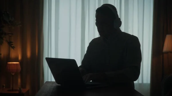 Темный Силуэт Человека Беспроводных Наушниках Столом Перед Ноутбуком Крупным Планом — стоковое фото