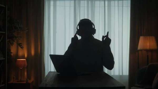 Ciemna Sylwetka Mężczyzny Słuchawkach Bezprzewodowych Przy Stole Przed Laptopem Człowiek — Zdjęcie stockowe