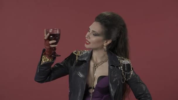 真正的女人穿着挑衅性的衣服 妆容光彩夺目 从手中的酒杯中吸入酒香 近照一个女人拿着一杯红酒的红色背景 — 图库视频影像