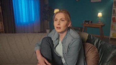 Genç bir kadın kanepede bacaklarıyla oturur ve akşamları televizyon izler. Bir kadın film, dizi, reality show izler, senaryoyu yakından takip eder, şaşırır ve başını sallar. HDR BT2020 HLG Malzemesi