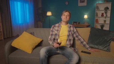 Bir adam yorucu bir iş gününden sonra bir bardak şarapla akşam kanepede televizyon karşısında dinleniyor. Bir adam kırmızı şarap içer ve film izlemekten zevk alır. HDR BT2020 HLG Malzemesi