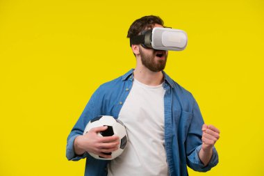 Mavi tişörtlü genç bir sakallı adamın portresi futbol topu tutma yasağı ve sanal gerçeklik gözlüğü takması. Başarı ifadesiyle yumruk sallamak. Maç izliyordum. İzole edilmiş